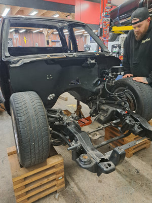 Car on a lift in a garage with a person working underneath.