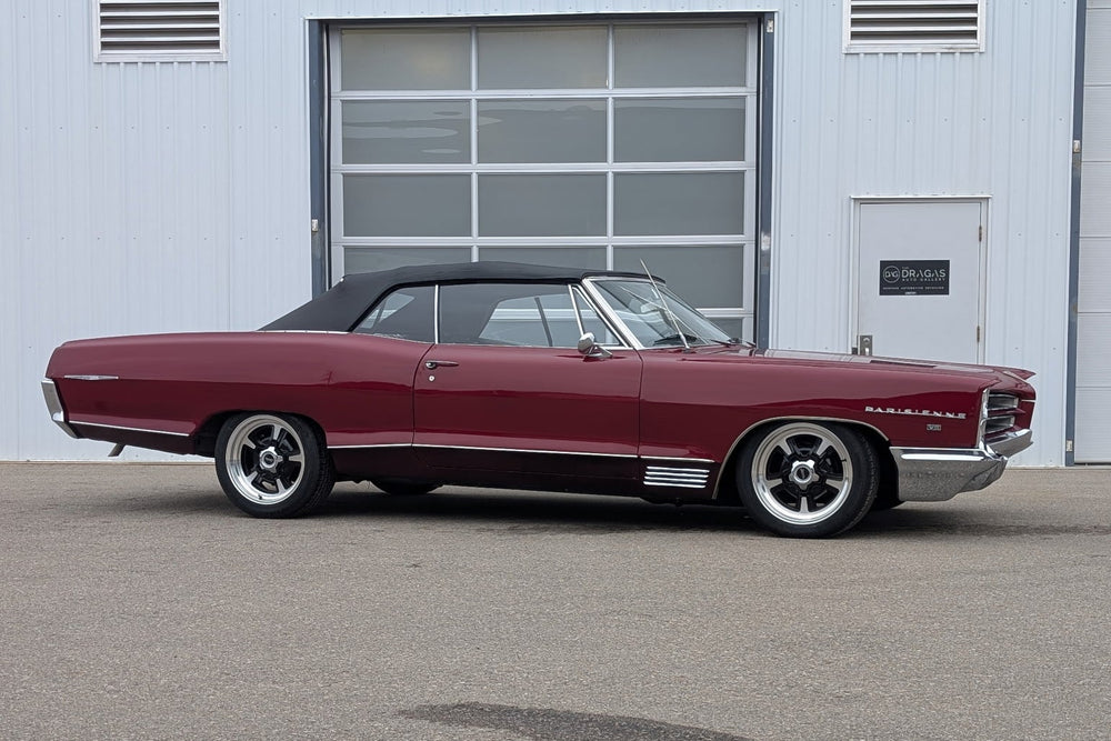Maroon classic Pontiac parked in front of a gray building with a garage door.