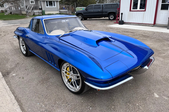Blue classic car parked on a driveway with a house and truck in the background
