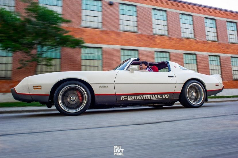 White convertible car with black stripes on a city street, blurred motion effect.