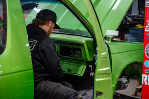 Person sitting inside a green vehicle with open door, possibly working on it.