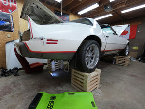 White Firebird with open hood on wooden blocks in a garage.