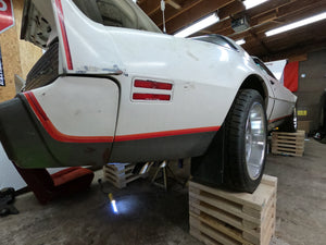 White car with red stripes on a wooden pallet in a garage.