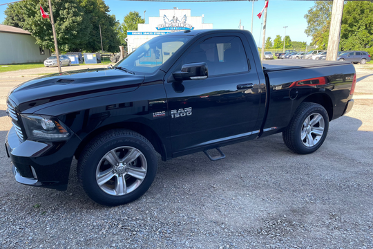 Black Ram truck parked on a gravel surface with a building and trees in the background.