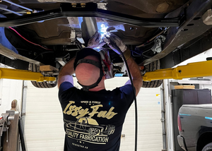 Person working on a vehicle undercarriage with a tig welder in a garage.