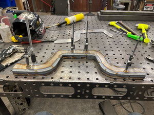 Metalworking setup with a welded crossmember on a workbench, surrounded by tools.
