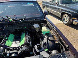 Open hood of a car showing engine components with another vehicle in the background.