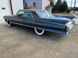 Vintage Cadillac parked on a concrete surface with a building and trees in the background