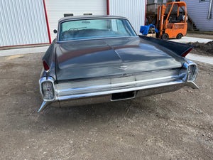 Vintage car parked on a concrete surface with a building and forklift in the background.