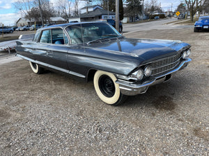 Vintage Cadillac parked on a street with buildings and trees in the background