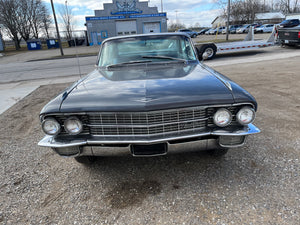 Vintage Cadillac parked on a gravel lot with a building and vehicles in the background