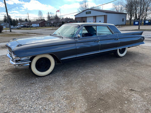 Vintage Cadillac parked on a gravel surface with a building and trees in the background