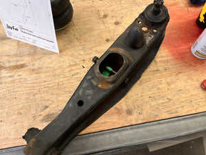 Lower Control Arm on a wooden surface with tools and a diagram in the background