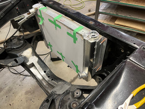 Metal radiator with green straps attached to a vehicle's engine bay.