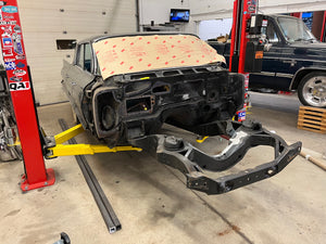 Car frame on a lift in a garage with various tools and equipment around