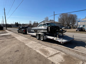 Car on a flatbed trailer being towed by a truck on a street.