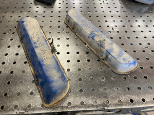 Two worn-out valve covers on a metal workbench