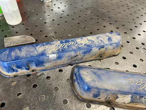 Two blue and worn-out engine covers on a metal workbench.