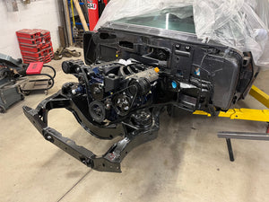 Car chassis on a lift in a garage setting with tools and equipment around.