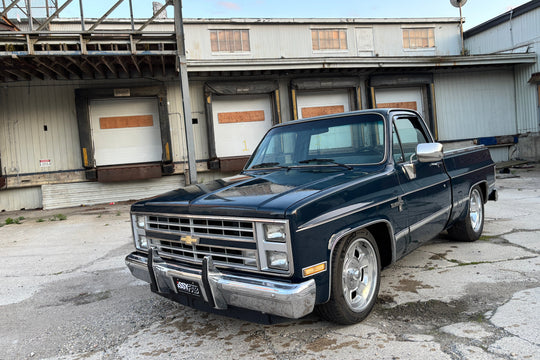 Vintage navy blue Chevrolet C10 truck parked in front of a warehouse.