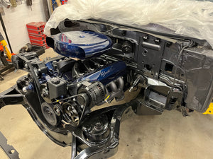 Car engine and mechanical components on a concrete floor with plastic sheeting in the background.