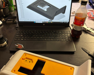 Laptop on a desk with a 3D model displayed, next to a yellow and white object.