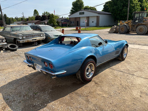Blue vintage car parked in a lot with other vehicles and buildings in the background