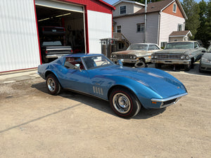 Blue classic 1969 Corvette parked in front of a garage with other cars in the background.