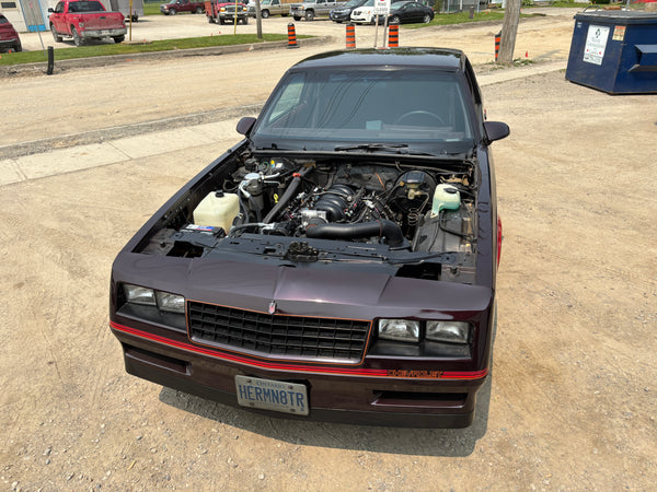 Car with its hood open on a concrete surface, likely in a parking lot.