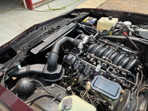 Car engine compartment with visible components on a concrete surface.