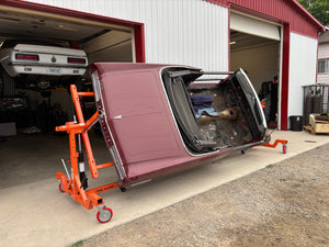Car on a rotisserie in front of a garage with another car inside