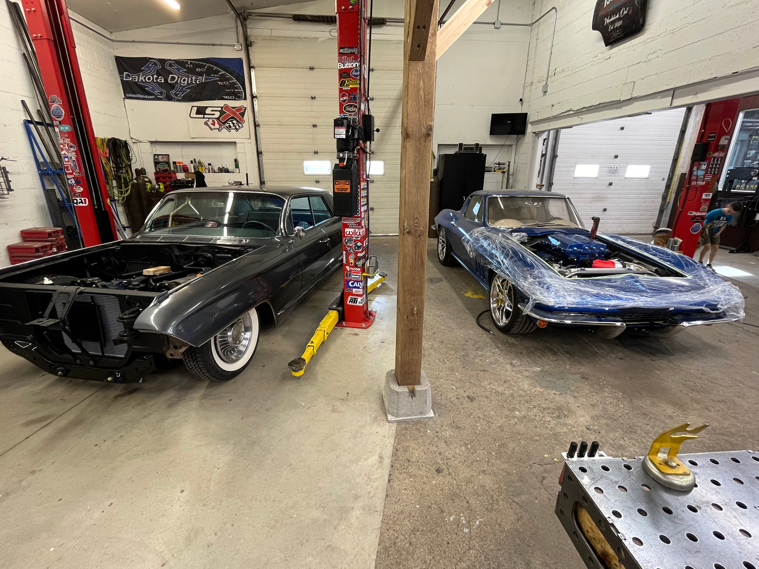 Two classic cars in a garage with one being worked on.