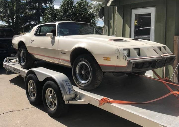 Vintage Firebird on a trailer in front of a house
