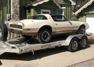 Vintage Firebird on a trailer in front of a green building with an awning.