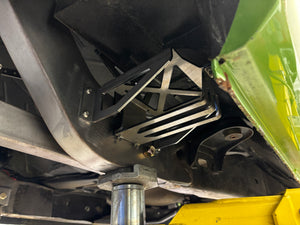 Close-up of a metal bracket on a vehicle's undercarriage with a yellow component in the background.