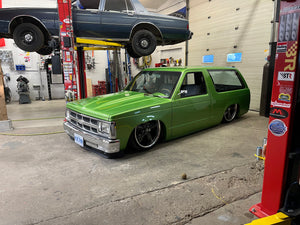 Green 1991 Jimmy in a garage with a car on a lift in the background