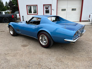 Blue vintage car parked in front of a white building with red trim
