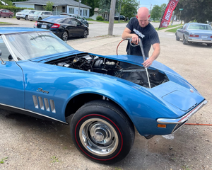 Man working on a blue vintage car in a parking lot.