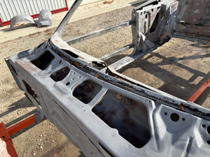 Metal car frame on a concrete surface with a red container in the background