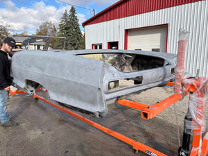 Car body on a rotisserie outside a building with a person in the foreground
