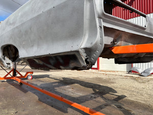 Car body on a lift with a red building in the background