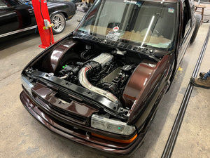 Car with its hood open, revealing the engine, on a concrete surface.