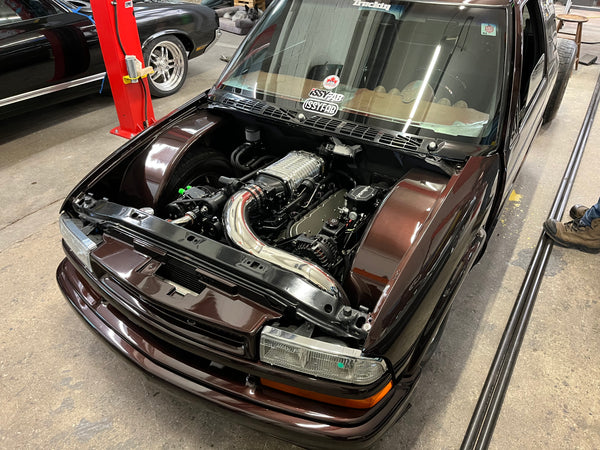Car with its hood open, revealing the engine, on a concrete surface.