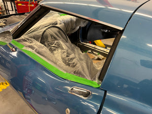Car with open hood covered by a plastic drop sheet, with green tape on the edge.