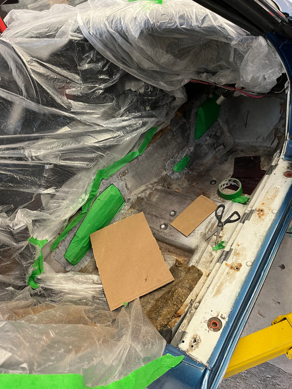 Car interior with plastic wrap, cardboard, and tools on a yellow lift.