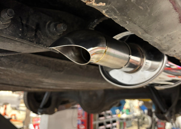 Close-up of a car exhaust system with a visible brand logo in a workshop setting.