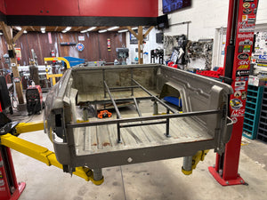 Metal truck bed on a lift in a workshop setting