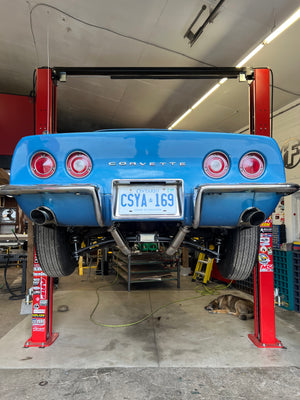 Blue Corvette on a lift in a garage with a dog sleeping nearby