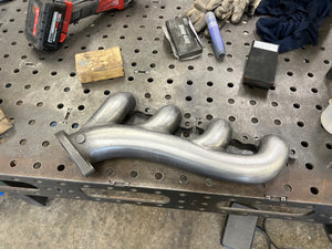 Metal exhaust manifold on a workbench with tools and equipment