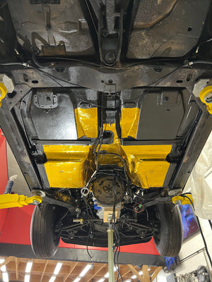 Undercarriage of a vehicle with yellow protective wrap in a workshop setting